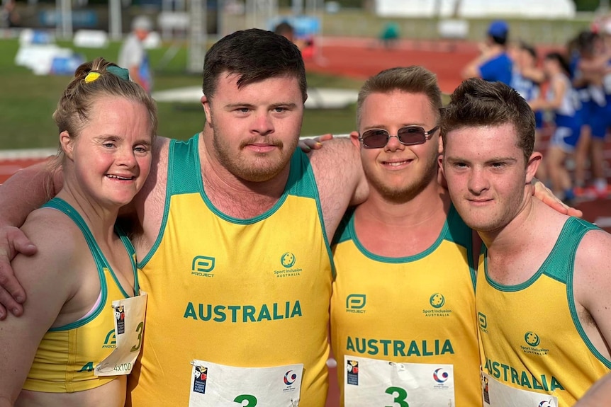 a group of athletes wearing yellow and gold uniforms stand trackside in an embrace 