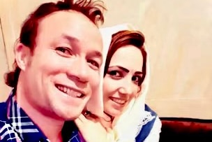 Young couple smiling as they take a selfie. He's wearing a dark blue check shirt and she has a head scarf on
