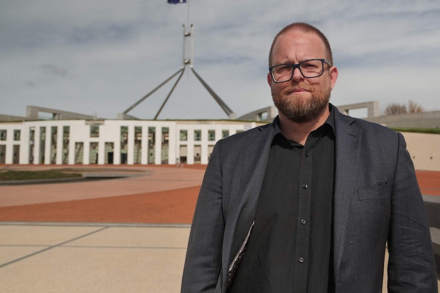 A man with glasses stands out the front of Parliament House.