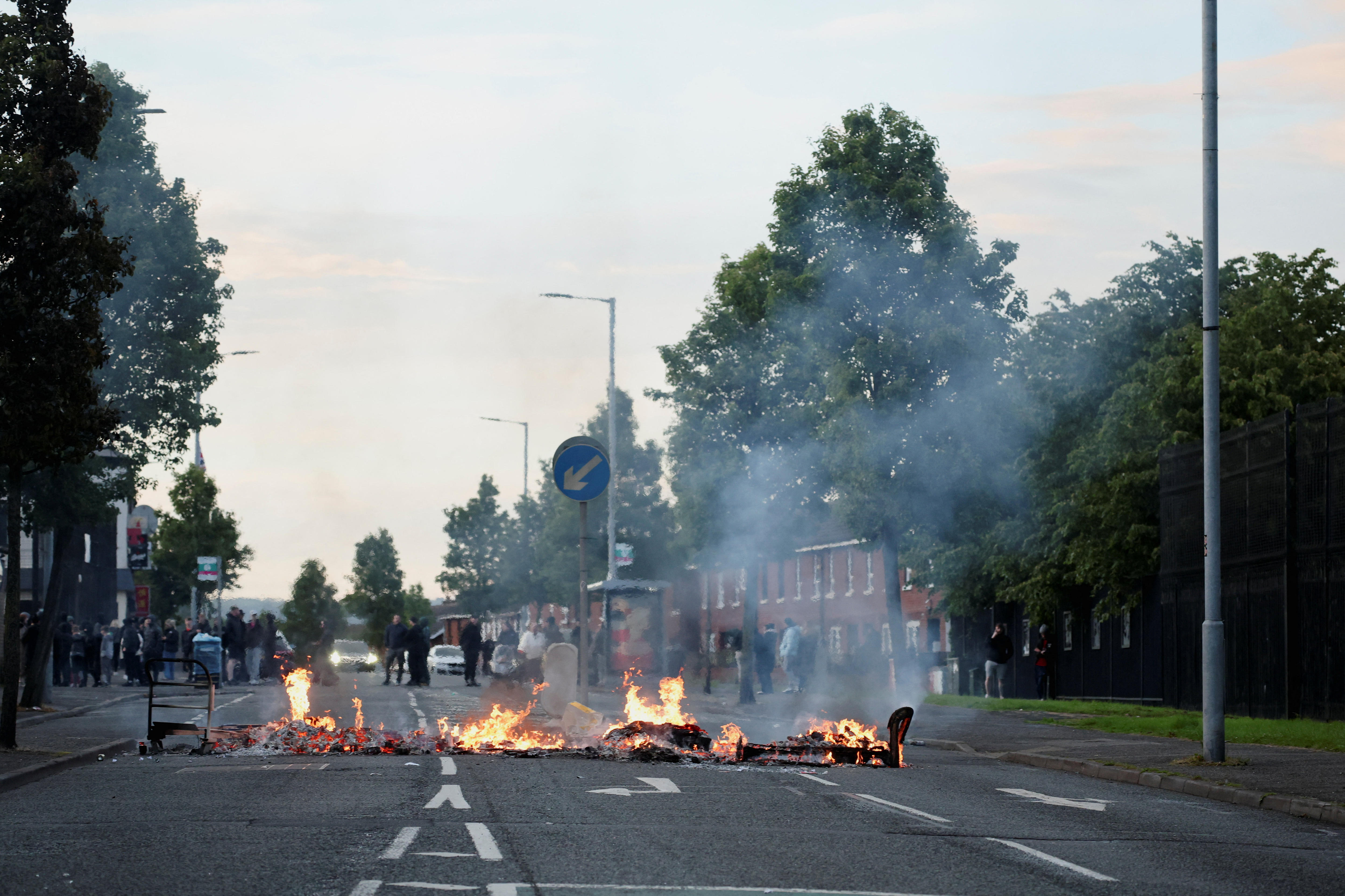 A fire burns on a street under a morning sky.