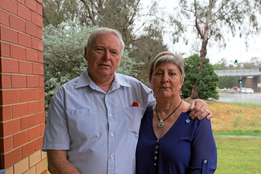 A man with white hair stands with his arm around his wife.