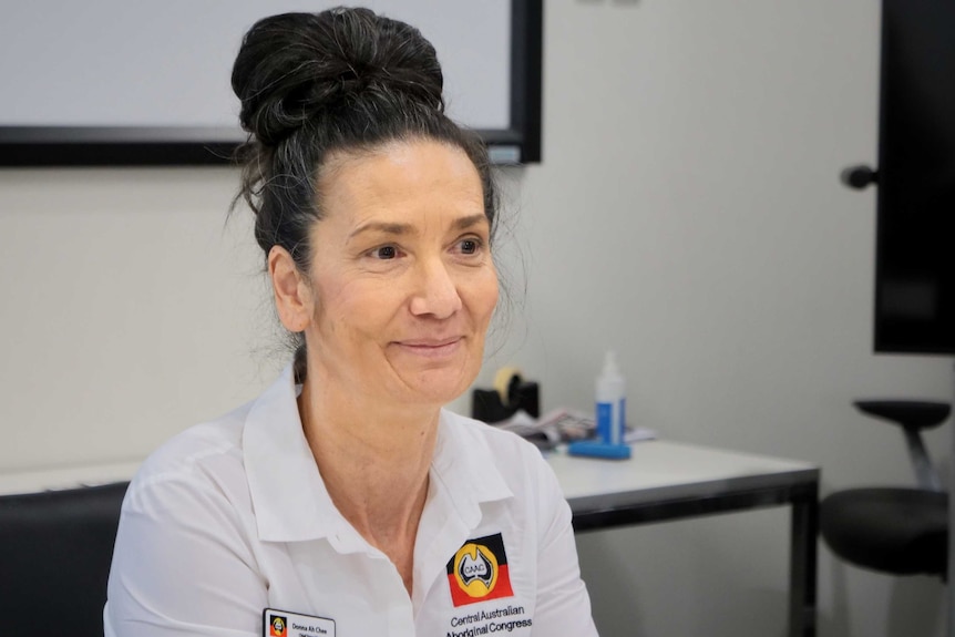 A middle-aged woman with her black hair done up in a bun sits in what appears to be an office space.