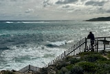 A man looks out over choppy surf from a viewing platform.
