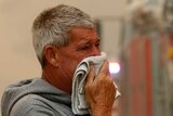 A man puts a towel on his face as he watches fire crews battle a bushfire