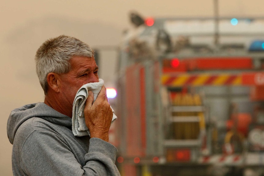 A man puts a towel on his face as he watches fire crews battle a bushfire