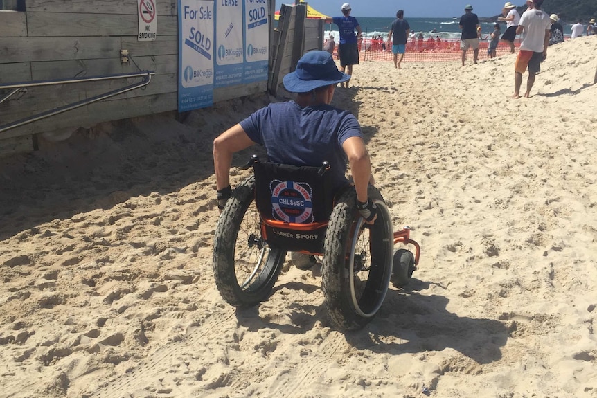 A man in a wheelchair propels himself over a sandy beach