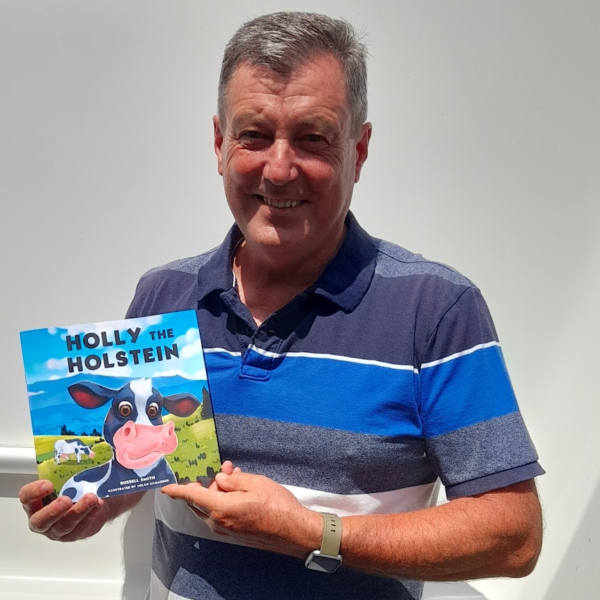 Russell Smith holds picture book with cow on it smiling. 