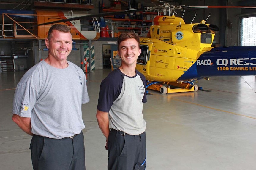 Two crew man standing in front of a helicopter grinning