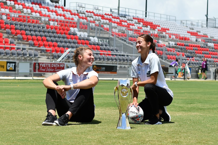 Jenna McCormick and Indiah-Paige Riley pose with the W-League trophy in a stadium