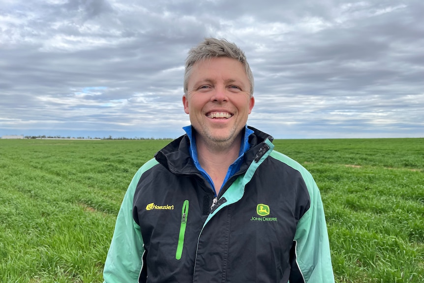 A smiling male farmer standing in a green field.