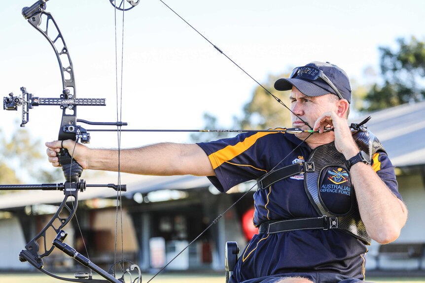 A man wearing a hat concentrates as he lines up a shot for archery