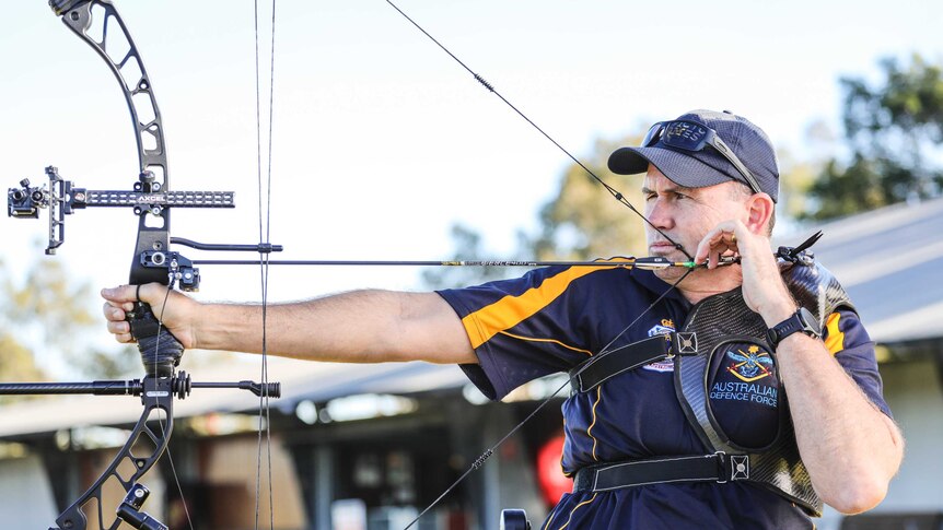 A man wearing a hat concentrates as he lines up a shot for archery