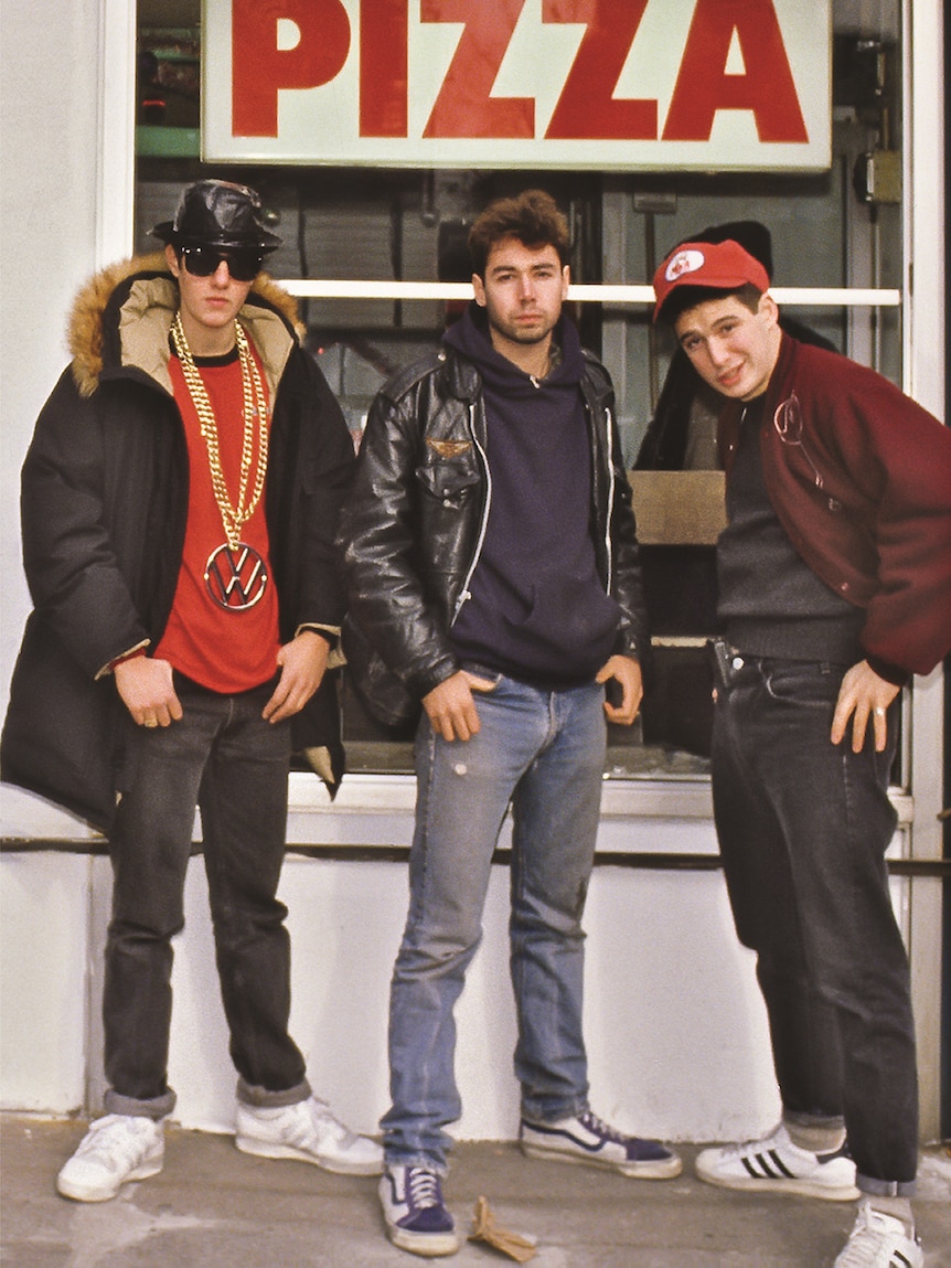 A book cover featuring colour film photograph of three men in jeans and jackets posing in front of pizza shopfront.