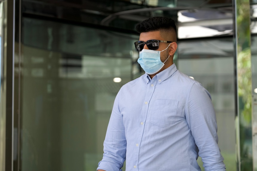 A man leaves court wearing a blue shirt, sunglasses and a mask