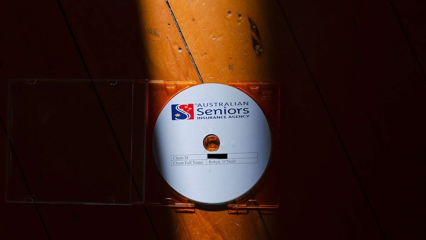 A CD sits in an orange case on a wood floor with a stream of light illuminating it. Dark either side of it.