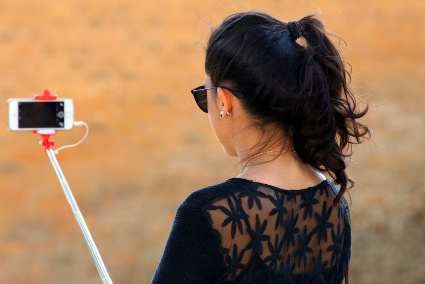 Woman taking photograph with a mobile phone and selfie stick.