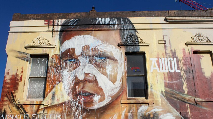 Street art in Fitzroy of Indigenous boy that takes up the entire side of an old yellow building.