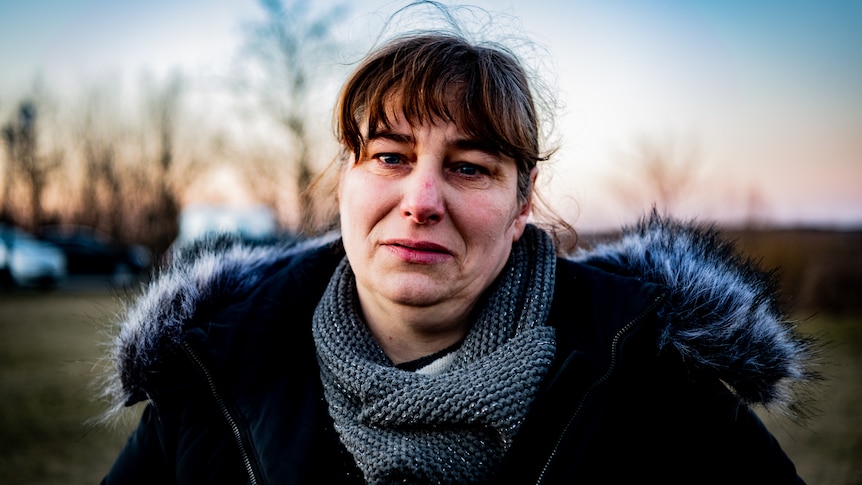 A woman in a fur trimmed coat looking frightened while standing in a field at sunset