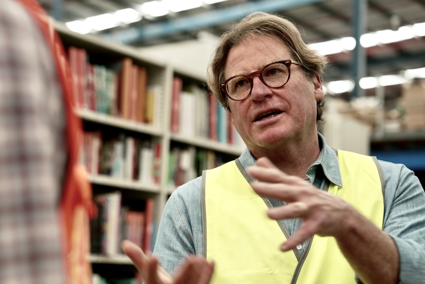 A man in a fluro yellow vest stands in front of shelves of books
