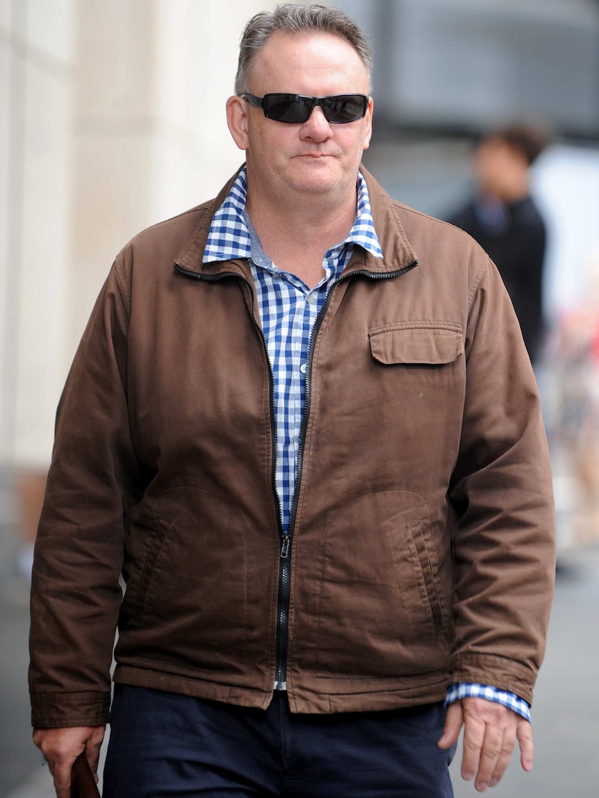 Mark Latham walks down the street wearing sunglasses.