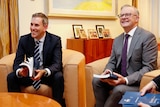 Jim Chalmers and Anthony Albanese sit on a couch holding the budget booklets. They are smiling.