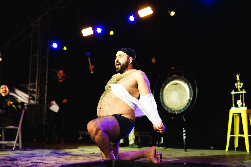 A man shows off his large bare belly on a stage with pride