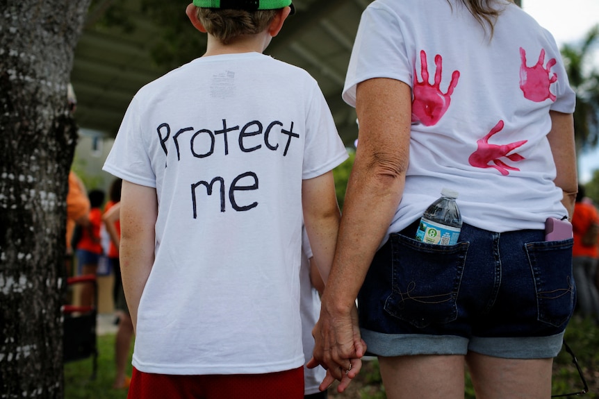 A boy with a shirt that reads 'protect me' and a woman with a shirt with children's handprints. 