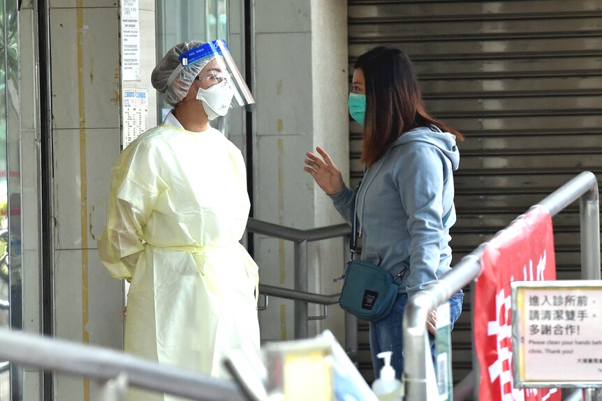A masked female patient speaks to a masked medical worker outside a medical clinic with Chinese signage