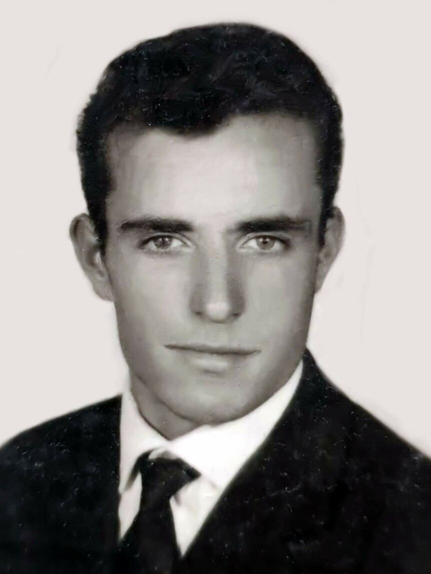 A young man in a suit looks at the camera.