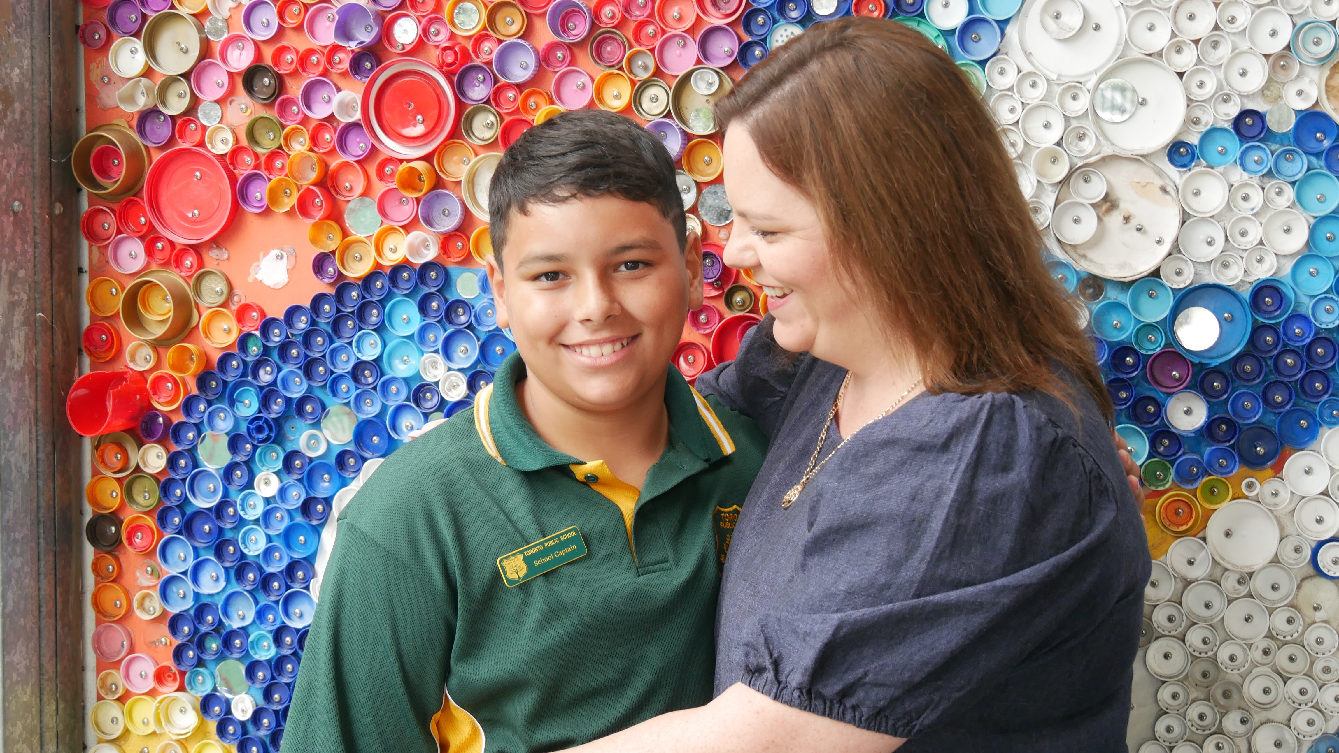 Jamahl and his mum Shanna hug in front of a rainbow wall at the school