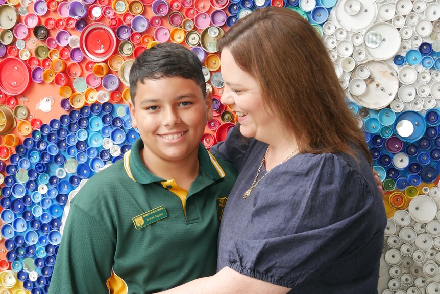 Jamahl and his mum Shanna hug in front of a rainbow wall at the school