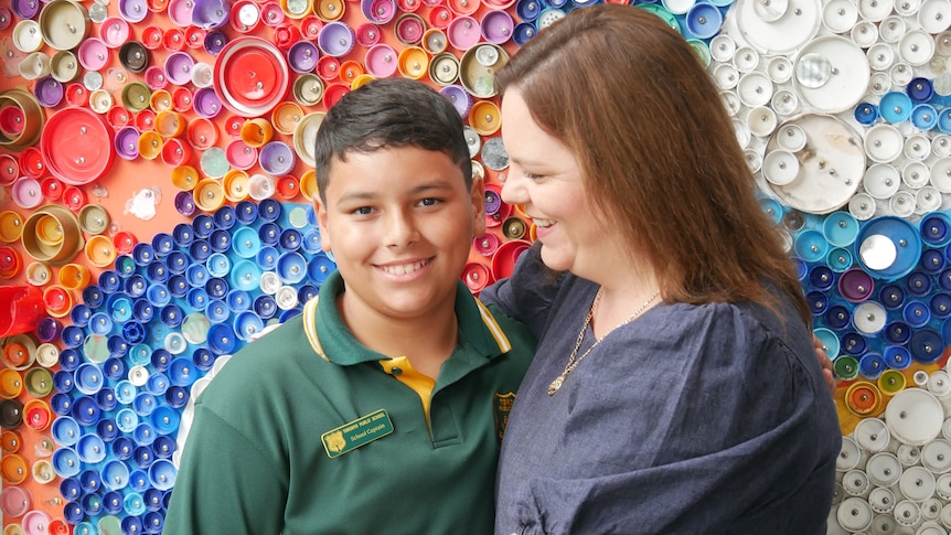 Jamahl and his mum Shanna hug in front of a rainbow wall at the school