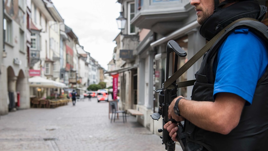 An armed officer stands in a street that has been shut down by police.