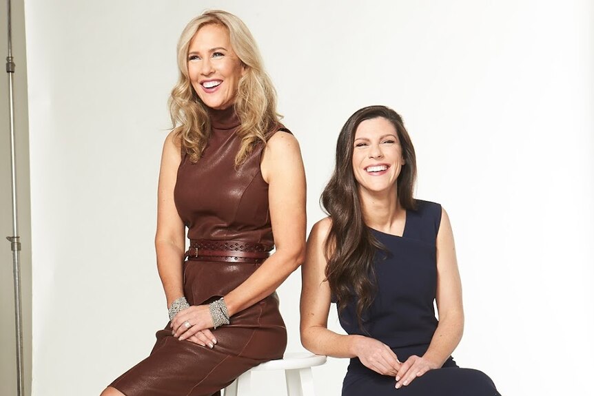 Two middle-aged women smile in a photography studio against a white backdrop.