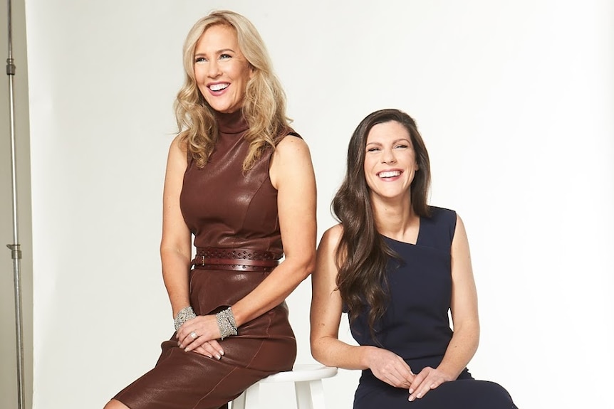 Two middle-aged women smile in a photography studio against a white backdrop.