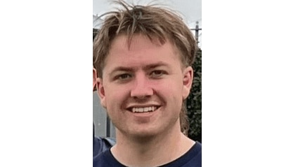 A photo of Samuel, smiling, in a blue t-shirt outdoors.