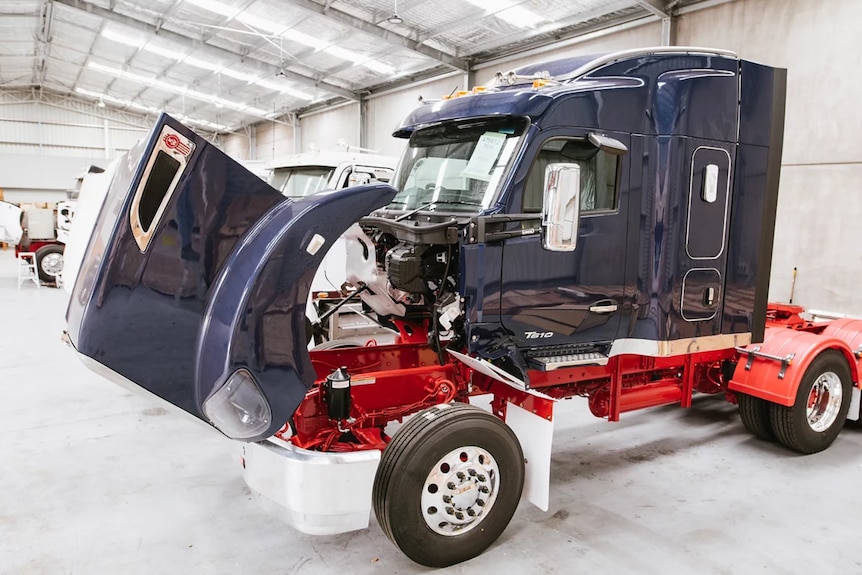 Blue and white prime mover in a factory with bonnet open, the engine has been removed ready for conversion to electric.