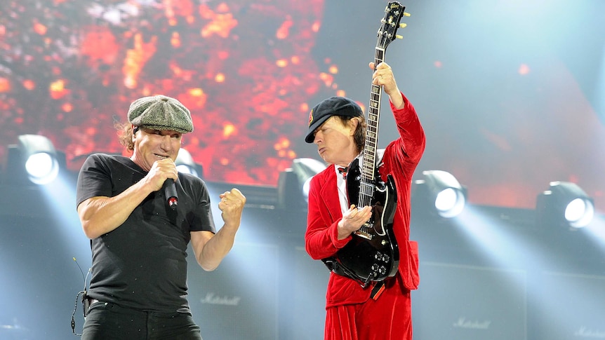 Brian Johnson, in trademark flat cap, and Angus Young, in red school uniform, perform next to each other onstage.