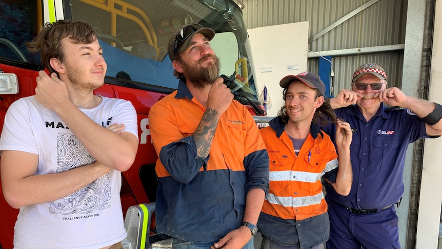 Josh Treffers, Peter Hooper, Shannon Beacom and Paul Clark stand in front of a fire truck and play with their own facial hair 