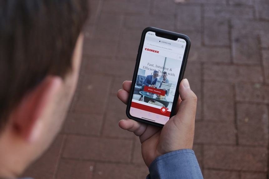 Nick Yeomans looks at a website advertising Coinexx on a phone.