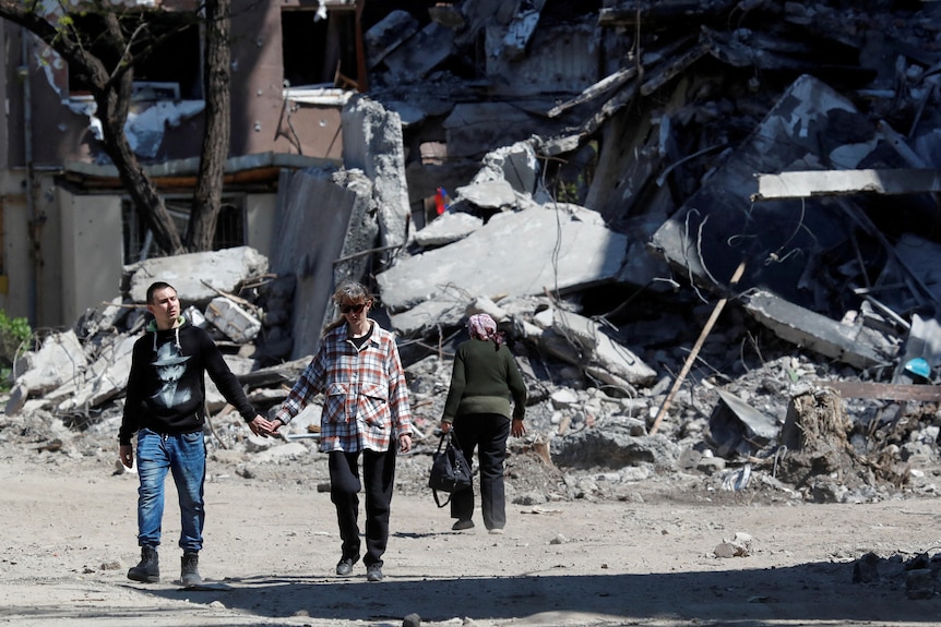 People walk by destroyed building.