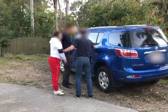 Two police officers hold a woman next to a car