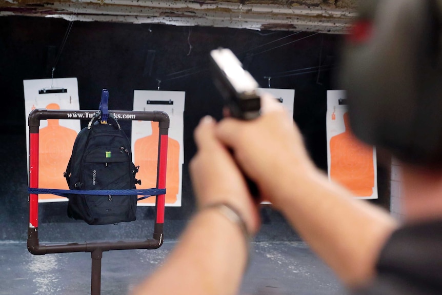 A man firing a handgun into a backpack at a shooting range.