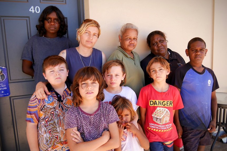 Three women and seven kids stand outside a motel door