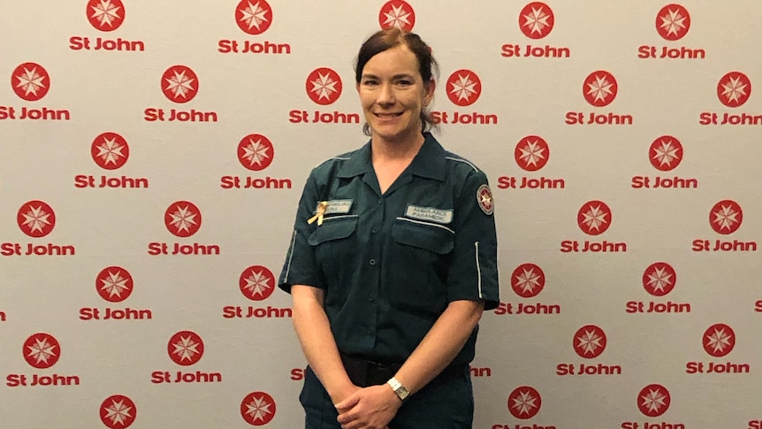 A woman wears her St John paramedic uniform and stands smiling for the camera.