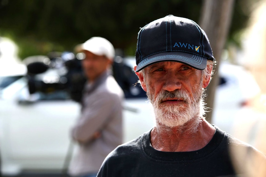 Headshot of a man wearing a cap with grey whiskers.