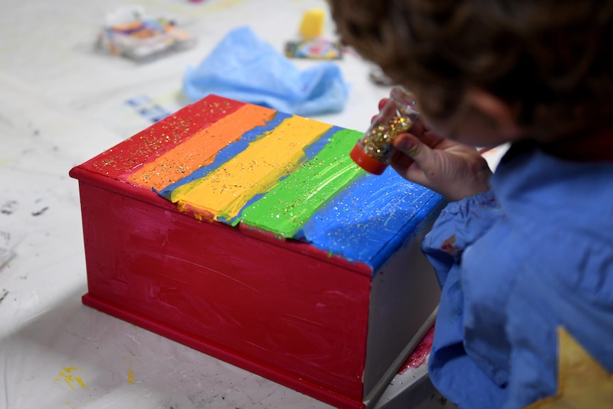 A child decorates a coloured box.