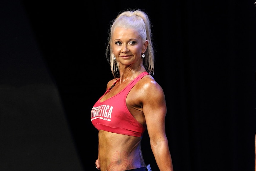 A woman with well-developed muscles poses on stage