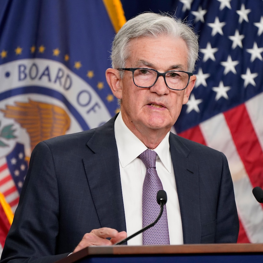Jerome Powell stands at a podium behind a wall of American flags. 
