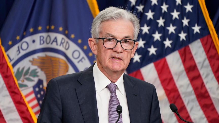 Jerome Powell stands at a podium behind a wall of American flags. 